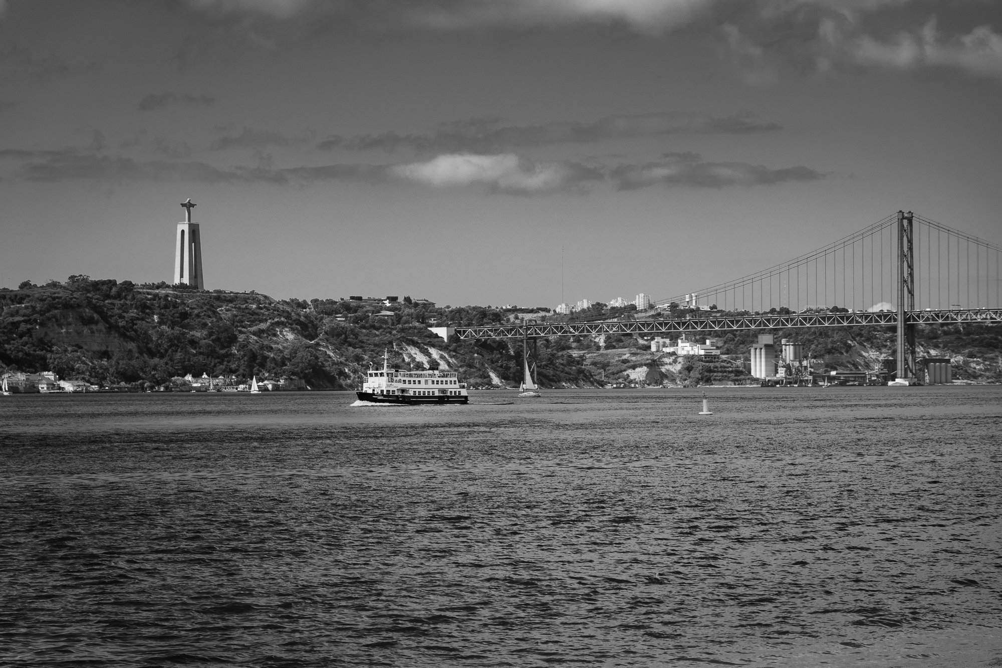Black and white view of a ferry on the Tagus in Lisbon, with Cristo Rei on the left and the 25 de Abril Bridge on the right