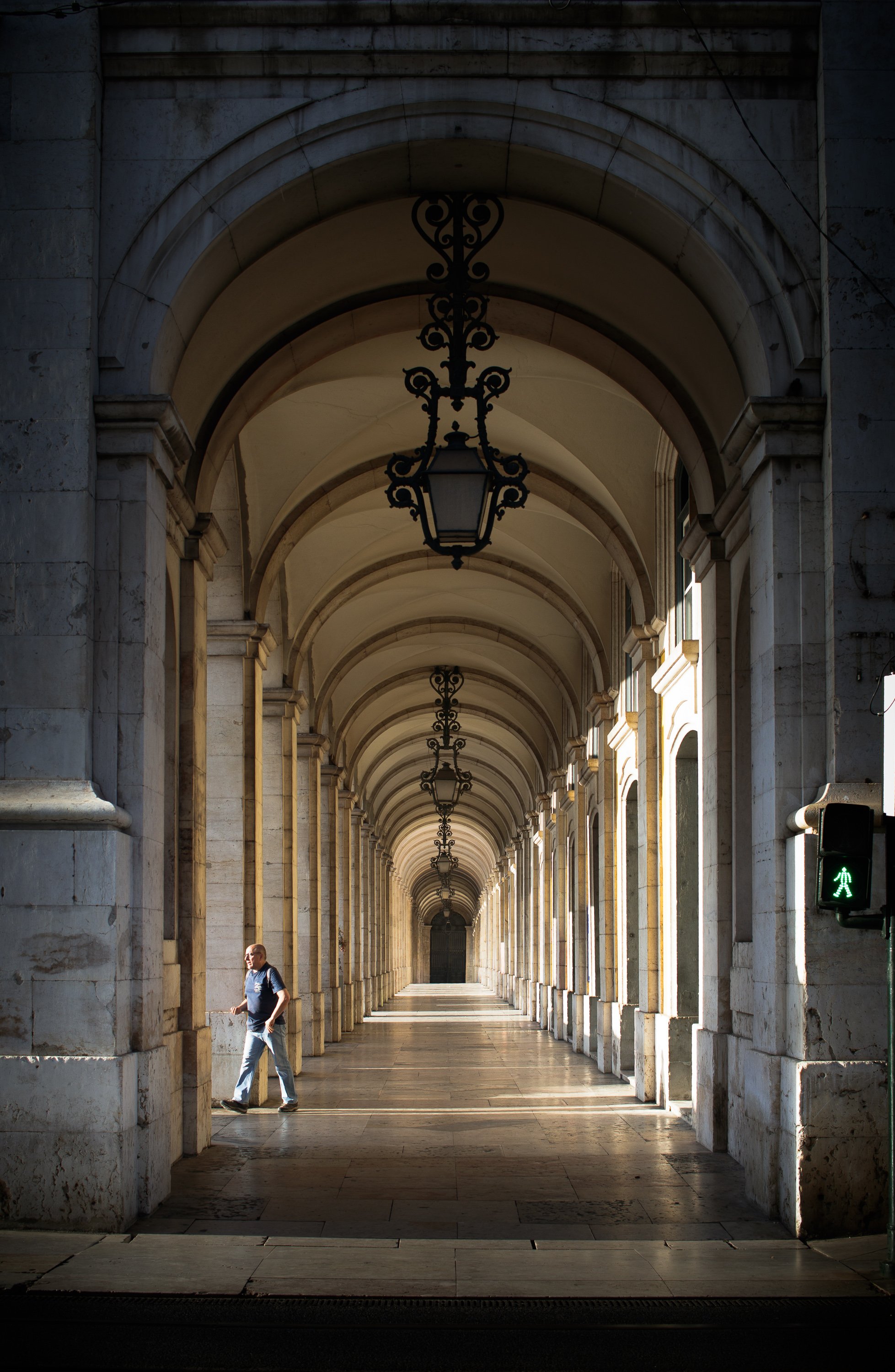 The arched colonnade of Praca do Comercio in Lisbon receding into golden light, with a man leaning against a stone column