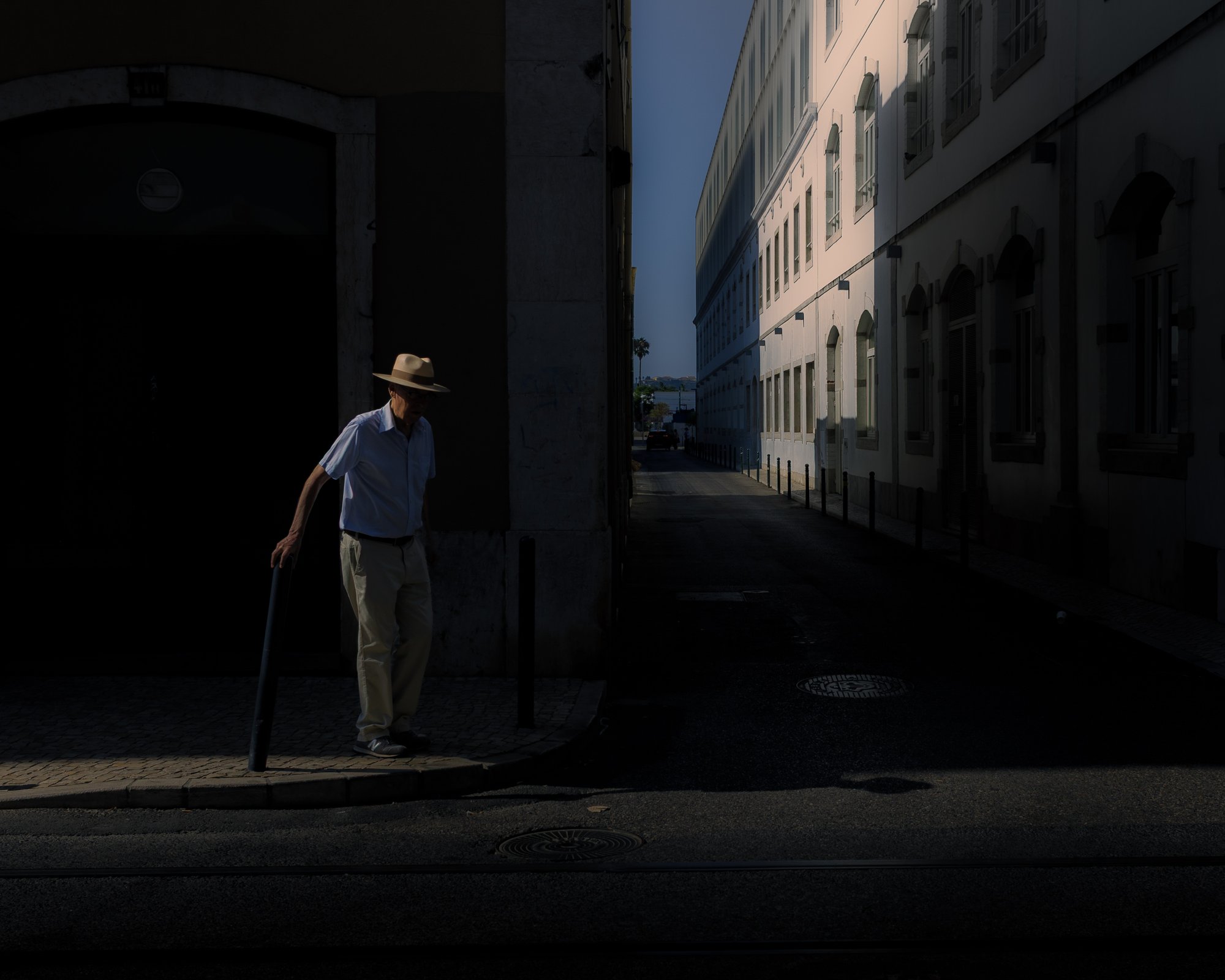 An elderly man in Panama hat lit by a single beam of light on a dark street corner near Cais do Sodré, Lisbon