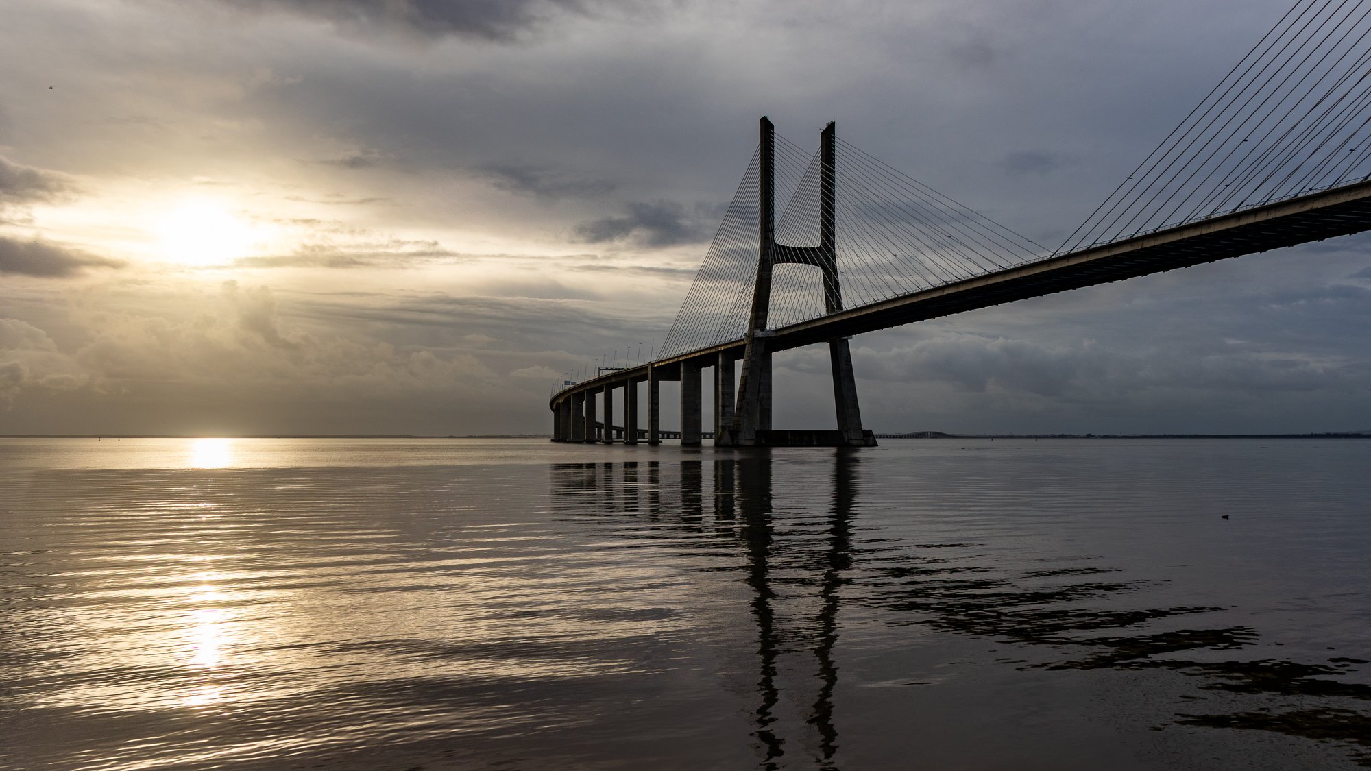 Vasco da Gama Bridge at sunrise, cable-stayed pylons reflecting on the calm surface of the Tejo river in Lisbon