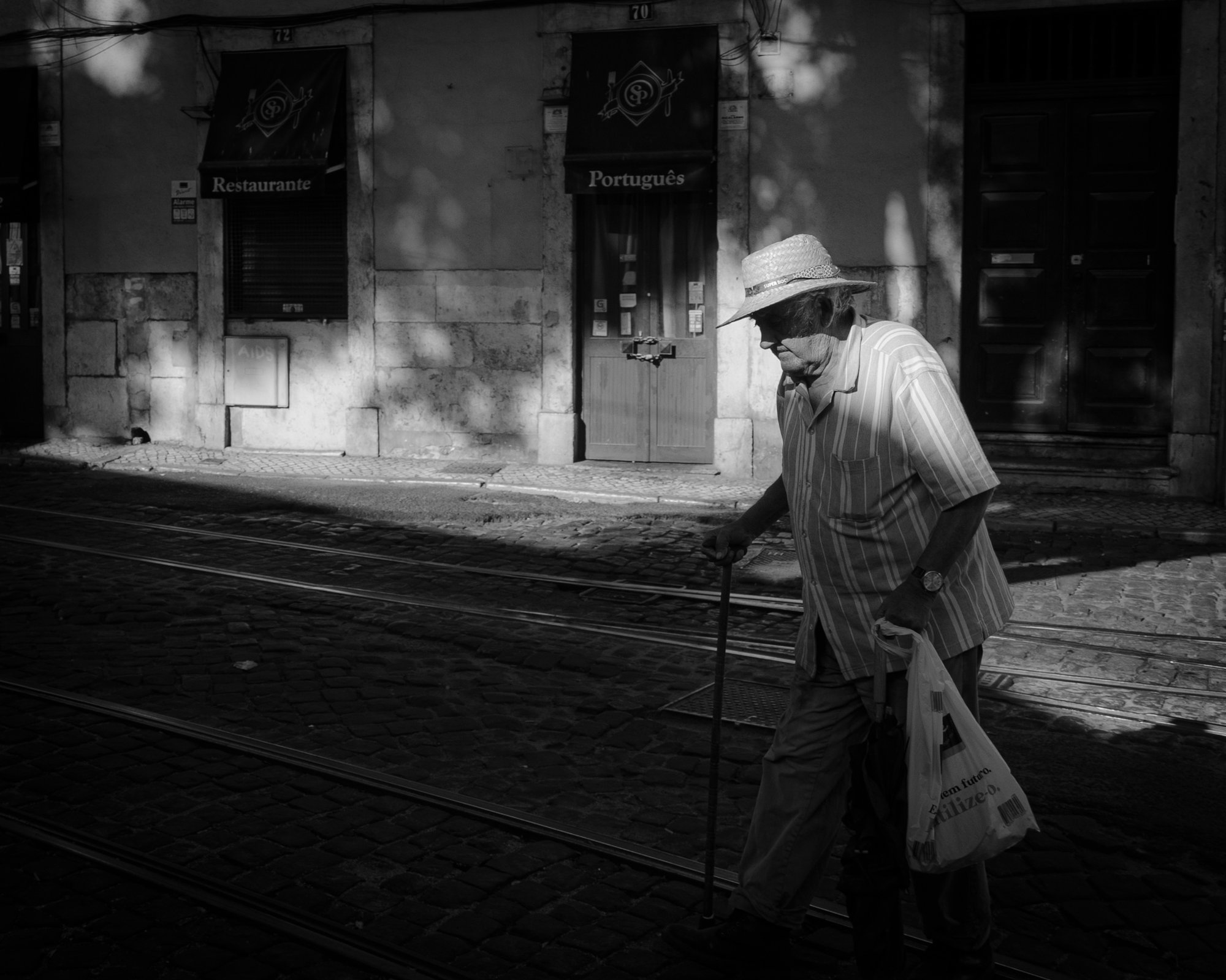 Person walking through a beam of sunlight beside tram tracks in Alfama, Lisbon